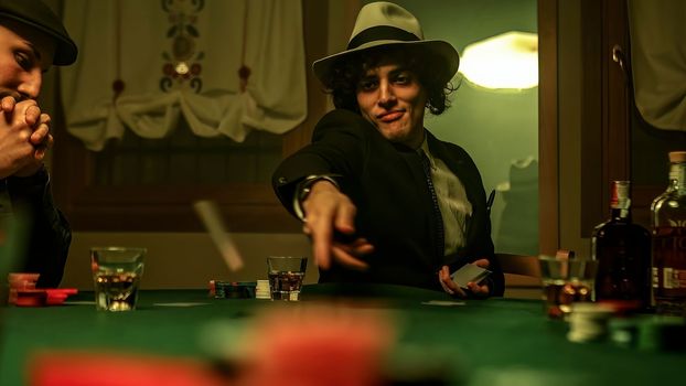 A group of mobsters gather around a table in a dimly lit nightclub. One of them who appears to be the leader of the group is distributing cards among the members to start a game of poker.