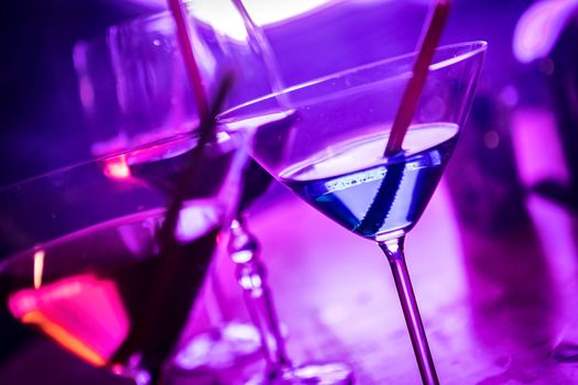 A variety of cocktail glasses in martini glasses are displayed on a bar top in a pub. The hands of people are shown holding the glasses. A variety of mixed alcoholic drinks are ready to be served.