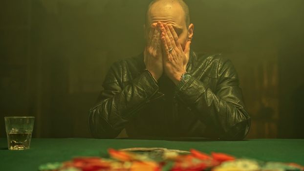 An excited poker player wins the game, reveals his cards while sipping whiskey and takes all the poker chips scattered on the table. Winning in gambling.