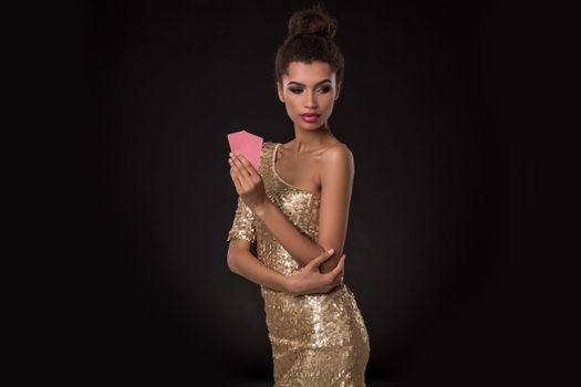 Woman winning - Young woman in a classy gold dress holding two cards, a poker of aces card combination. Studio shot on black background. Emotions