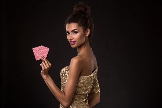 Woman winning - Young woman in a classy gold dress holding two cards, a poker of aces card combination. Studio shot on black background. A young woman stands with her back