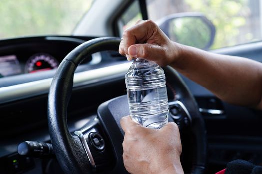 Asian woman driver hold cold water for drink in car, dangerous and risk an accident.