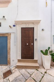 View of the empty streets of old town Martina Franca with a beautiful houses painted in white among greenery. Wonderful cactus in the pot at the front door. Nice day in a tourist town, Apulia, Italy.