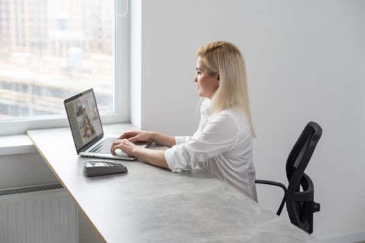 Image of young pleased happy cheerful cute beautiful business woman sit indoors in office using laptop computer.