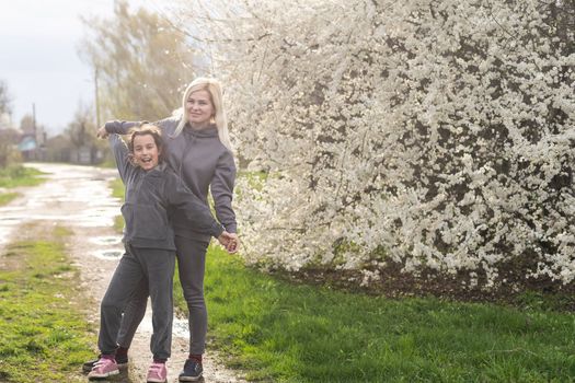 Woman walking with daughter in blooming spring garden exploring flowering tree. Family admires nature