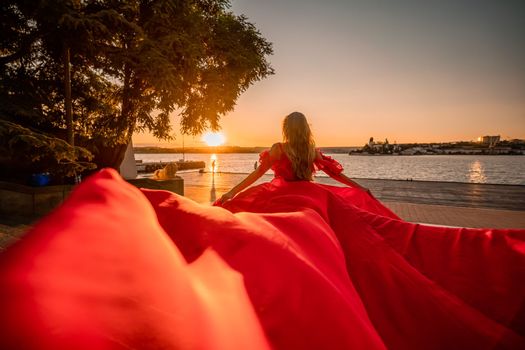 Sunrise red dress. A woman in a long red dress against the backdrop of sunrise, bright golden light of the sun's rays. The concept of femininity, harmony