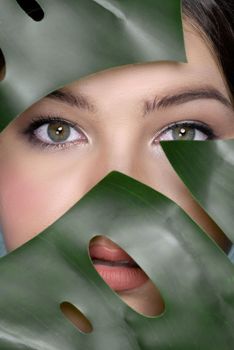 Portrait of young woman face surrounded with tropical green leaves. Healthy clean and perfect smooth skin of charming young woman. Natural beauty cosmetic and wellness concept for skincare product.