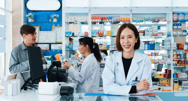Portrait of affable asian pharmacist and qualified pharmaceutical, medicine pill bottle on shelf in background at pharmacy. Concept of pharmacist working on cashier talking to customer in drugstore.