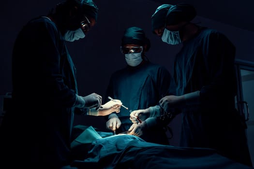 Surgical team performing surgery to patient in sterile operating room. In a surgery room lit by a lamp, a professional and confident surgical team provides medical care to an unconscious patient.