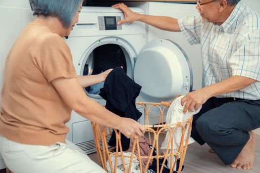 Senior couple working together to complete their household chores at the washing machine in a happy and contented manner. Husband and wife doing the usual tasks in the house.