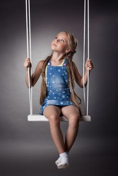 Studio portrait of beautiful blonde girl on swing