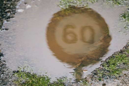 Close up speed limit road sign on an urban street reflected in a puddle of water