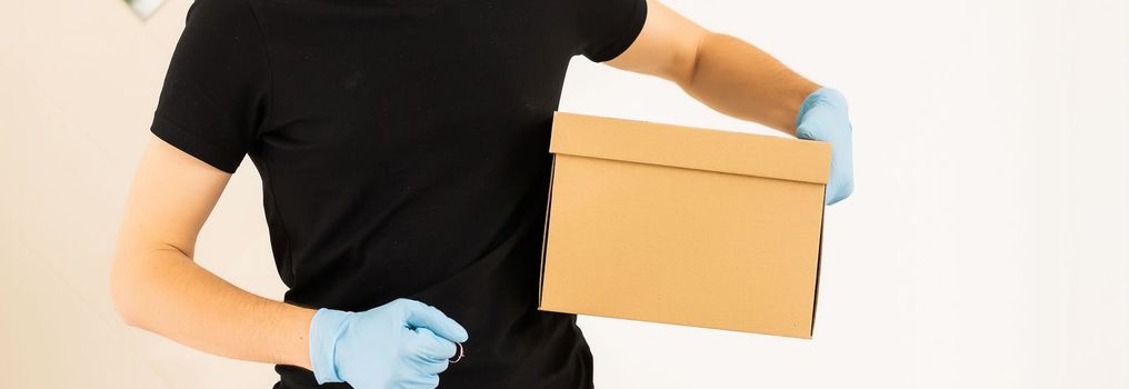 delivery man holding package to deliver. Courier hand holding brown box isolated on grey background. Detail of delivery man carrying cardboard parcel with label with copy space