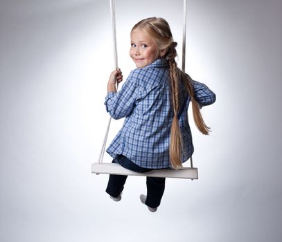 Studio portrait of beautiful blonde girl on swing