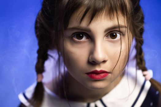 Portrait of a young girl isolated on blue background. Beautiful girl looking at camera. Face gothic child girl. Closeup portrait of a beautiful sad girl in color tones.