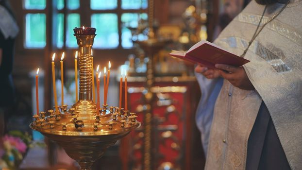 Burning candles against the background of the Priest reading the Bible at the service