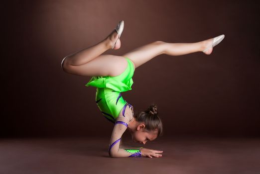 small girl gymnast stand on hands in green costume