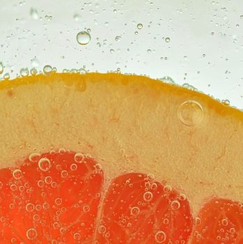 Close-up view of the red grapefruit slice in water background. Texture of cooling fruit drink with macro bubbles on the glass wall. Flat design.