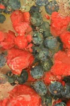 Water with fresh berries, close-up. Close-up view of the blueberries and raspberries in water background. Texture of bilberries and raspberries with macro bubbles on the glass wall. Flat design, top view. Vertical image. Defocused.