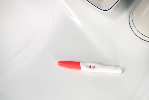 View from above. Selective focus on an inkjet pregnancy test in action with positive result on a white wahbasin in the home bathroom.