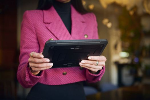 Details on digital tablet in the hands of a restaurateur, businesswoman in bright purple casual wear, executive director or successful manager, CEO against blurred background of a restaurant interior