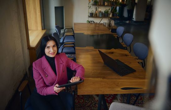 Confident, attractive, successful, goal-oriented middle-aged Caucasian woman, chief executive, business woman sitting with a tablet at the table and waiting for a meeting with partners and investors