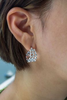 Detail of young woman wearing beautiful silver earring. Women accessories. Selective focus.