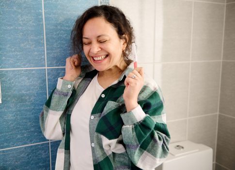 Middle-aged pretty woman rejoicing at positive pregnancy test, standing on the light interior of home bathroom. Pregnancy, people, lifestyle concept