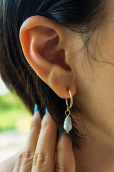 Detail of young woman wearing beautiful golden earring white pearl. Women accessories. Selective focus.