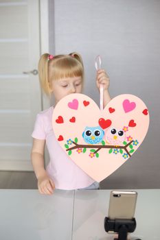 A blogger girl makes a felt craft for Valentine's Day in the shape of a heart. The concept of children's creativity and handmade