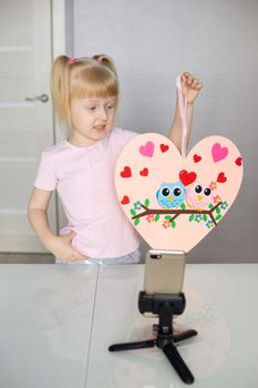 A blogger girl makes a felt craft for Valentine's Day in the shape of a heart. The concept of children's creativity and handmade