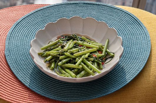 Stir-Fried Chinese Morning Glory or Water Spinach (pak boong fai daeng) seasoned with chili and soy sauce on white plate. Asian food style, Selective focus.