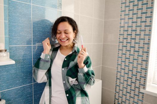 Middle-aged smiling woman with positive pregnancy test in the home bathroom