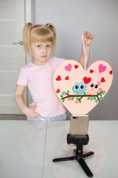 A blogger girl makes a felt craft for Valentine's Day in the shape of a heart. The concept of children's creativity and handmade