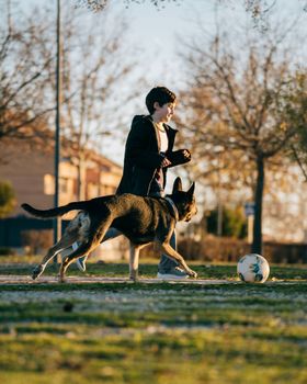 Selective focus in motion. Kid playing football with dog in a park.