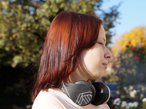 portrait in profile of a red-haired teenage girl with headphones on a background of nature.