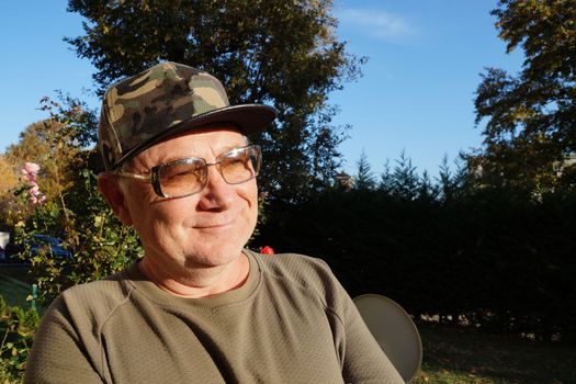portrait of a smiling man in sunglasses and a baseball cap in the sunlight in the park.