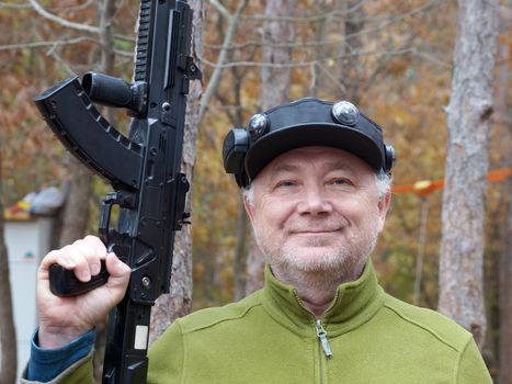 portrait of a smiling adult man with a laser game weapon in his hands in the forest.