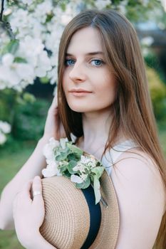 Beautiful young girl in white dress and hat in blooming Apple orchard. Blooming Apple trees with white flowers