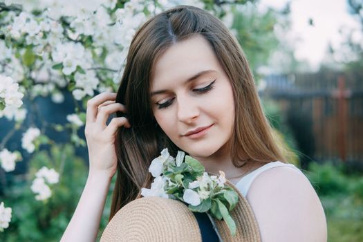 Beautiful young girl in white dress and hat in blooming Apple orchard. Blooming Apple trees with white flowers