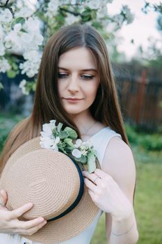 Beautiful young girl in white dress and hat in blooming Apple orchard. Blooming Apple trees with white flowers