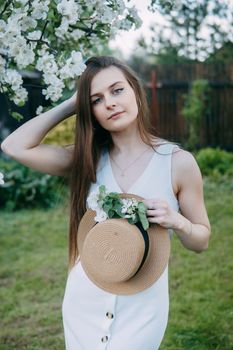 Beautiful young girl in white dress and hat in blooming Apple orchard. Blooming Apple trees with white flowers