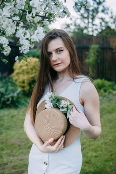 Beautiful young girl in white dress and hat in blooming Apple orchard. Blooming Apple trees with white flowers