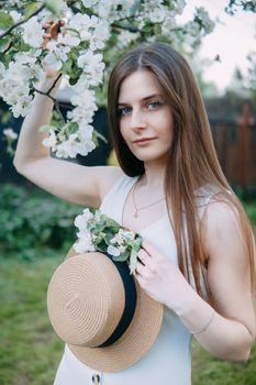 Beautiful young girl in white dress and hat in blooming Apple orchard. Blooming Apple trees with white flowers