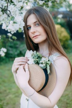 Beautiful young girl in white dress and hat in blooming Apple orchard. Blooming Apple trees with white flowers