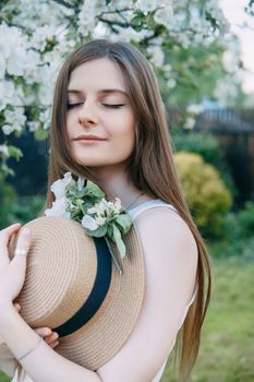 Beautiful young girl in white dress and hat in blooming Apple orchard. Blooming Apple trees with white flowers