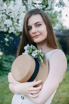 Beautiful young girl in white dress and hat in blooming Apple orchard. Blooming Apple trees with white flowers