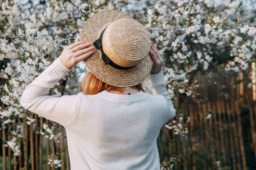Portrait of a woman in a straw hat in a cherry blossom. Free outdoor recreation, spring blooming garden.