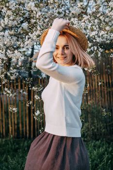 Portrait of a woman in a straw hat in a cherry blossom. Free outdoor recreation, spring blooming garden.