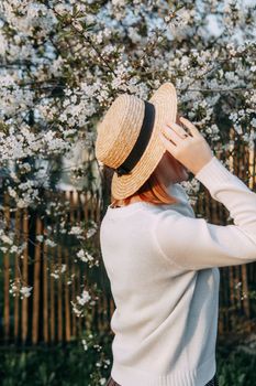 Portrait of a woman in a straw hat in a cherry blossom. Free outdoor recreation, spring blooming garden.